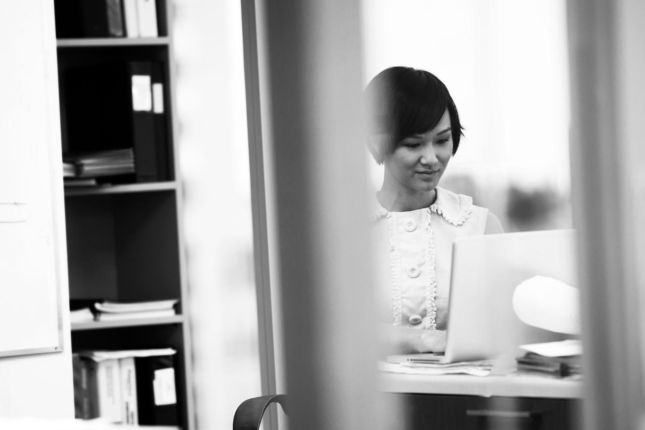 A black and white photo of a young lady sitting in her office working on a laptop