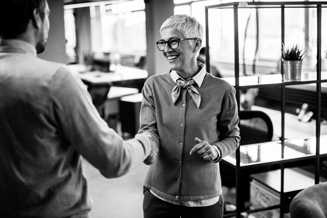 Young business man and senior business woman shaking hands in the modern office