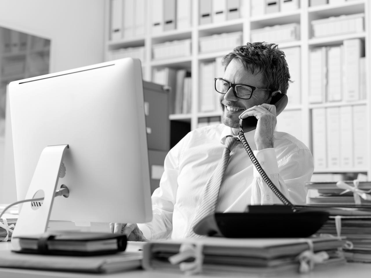 A man talking on the telephone while sitting in front of a computer