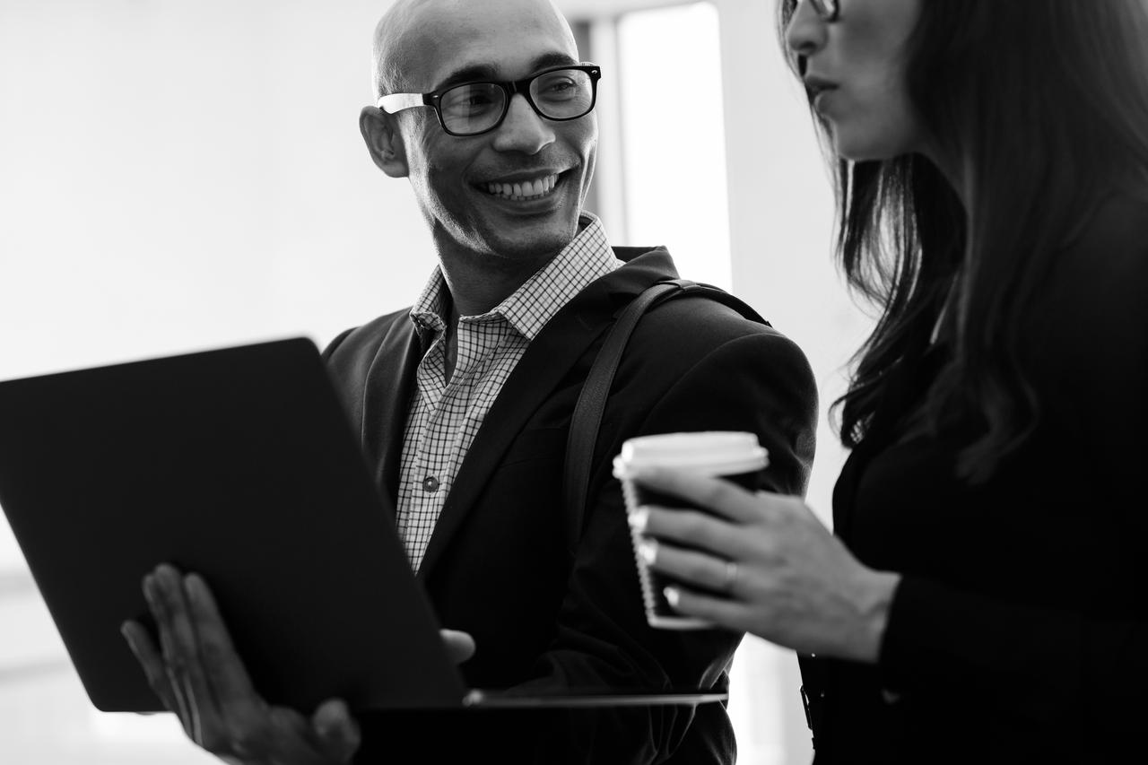 Smiling businessman holding laptop looking at female colleague in office