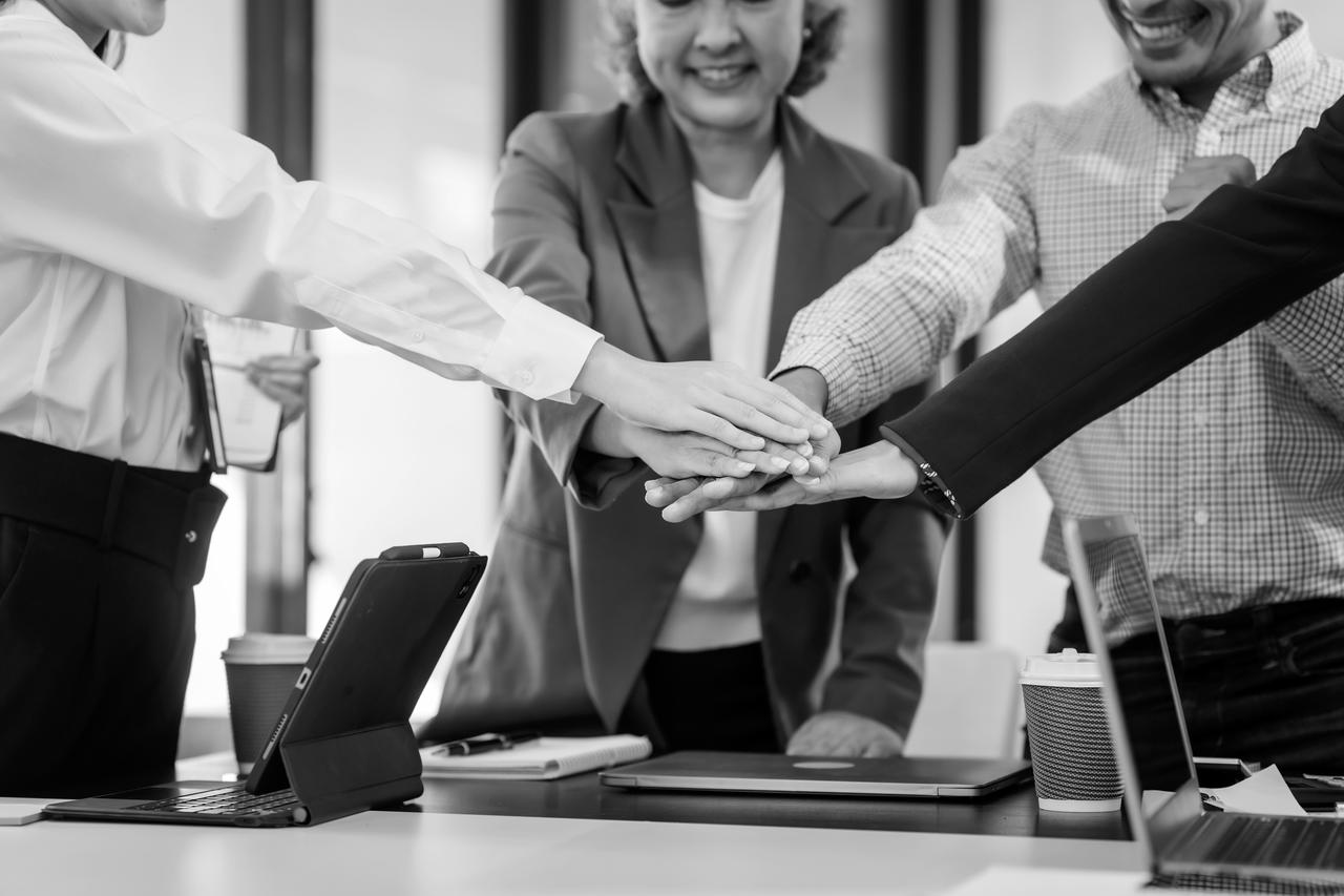 Four people in an office put their hands together as a team.