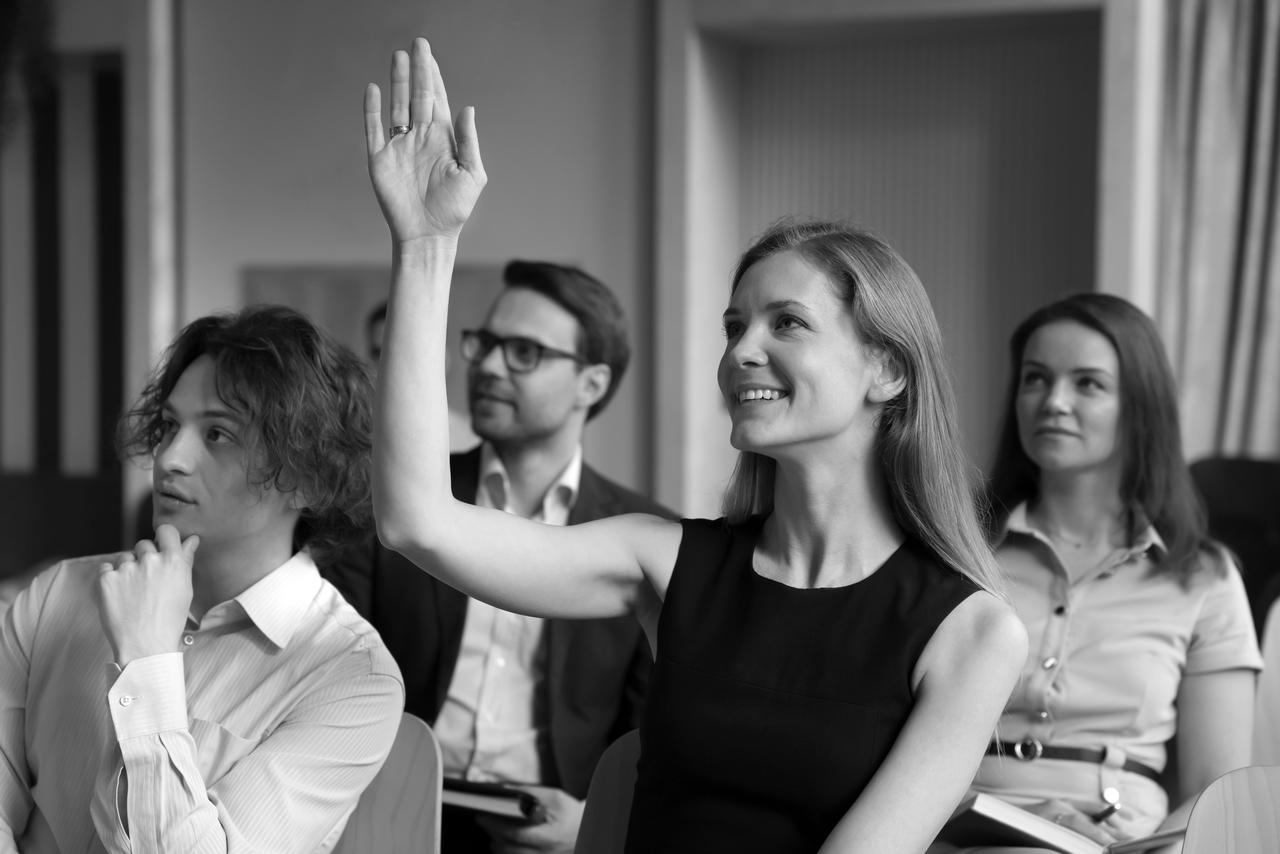 Smiling woman sitting in a crowd with her hand raised