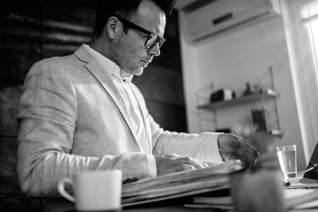 Businessman wearing linen suit and eyeglasses sitting at his desk searching files