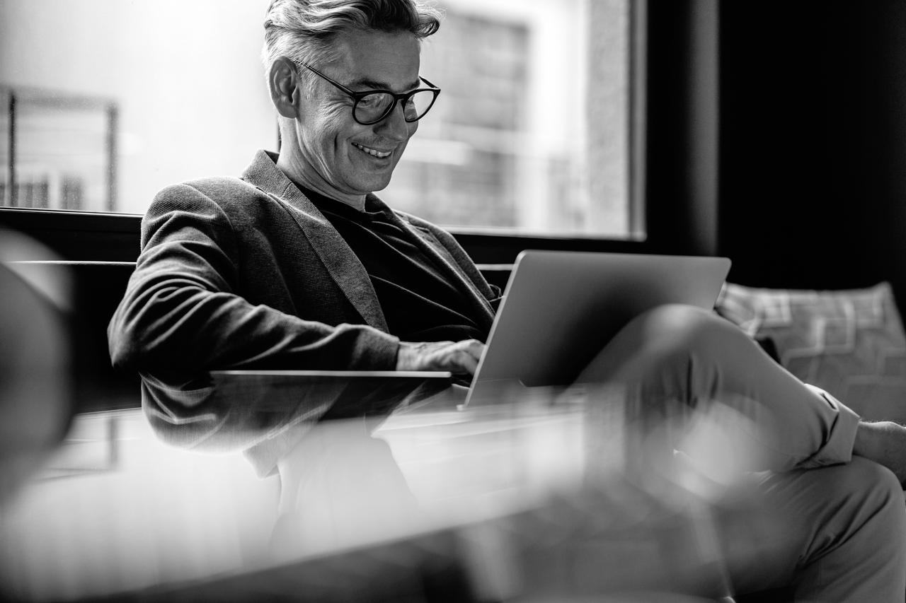 Smiling businessman sitting in office lobby working on a laptop