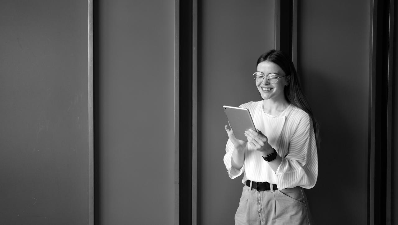 A young lady holding a tablet and standing against a wall